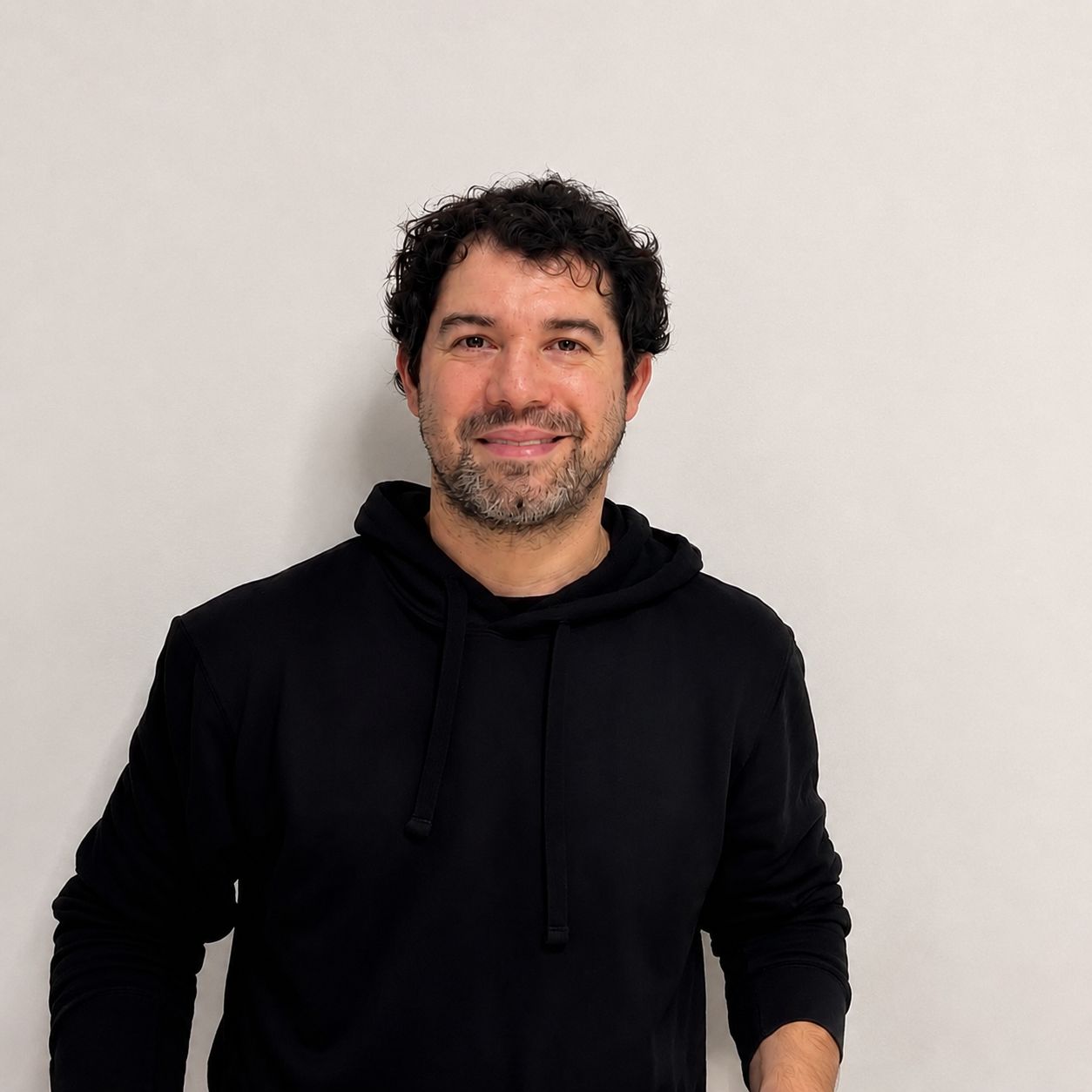 Agustín sonriendo, con buzo negro sobre un fondo claro