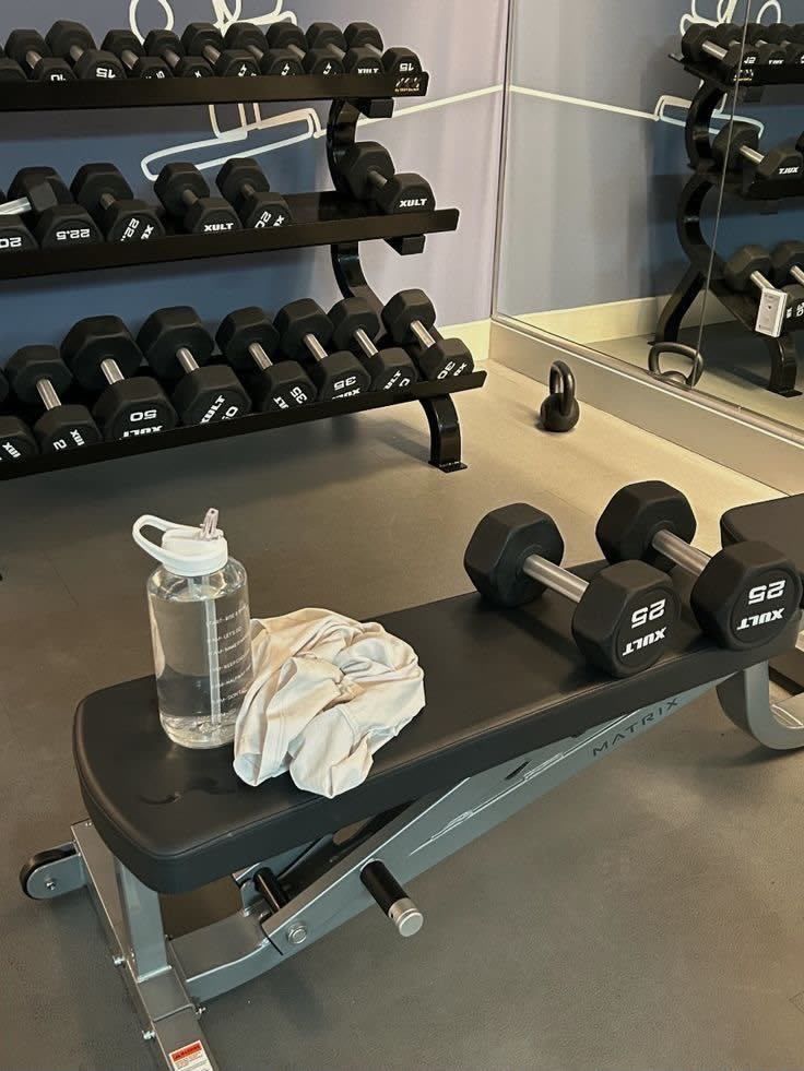 Banco de gimnasio con mancuernas, botella de agua y toalla